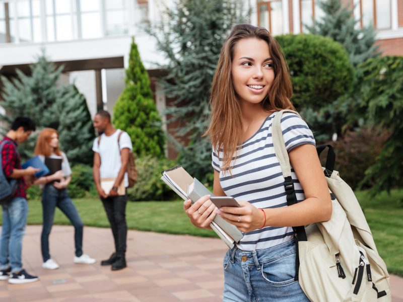 Happy woman student with backpack holding books and walking outdoors